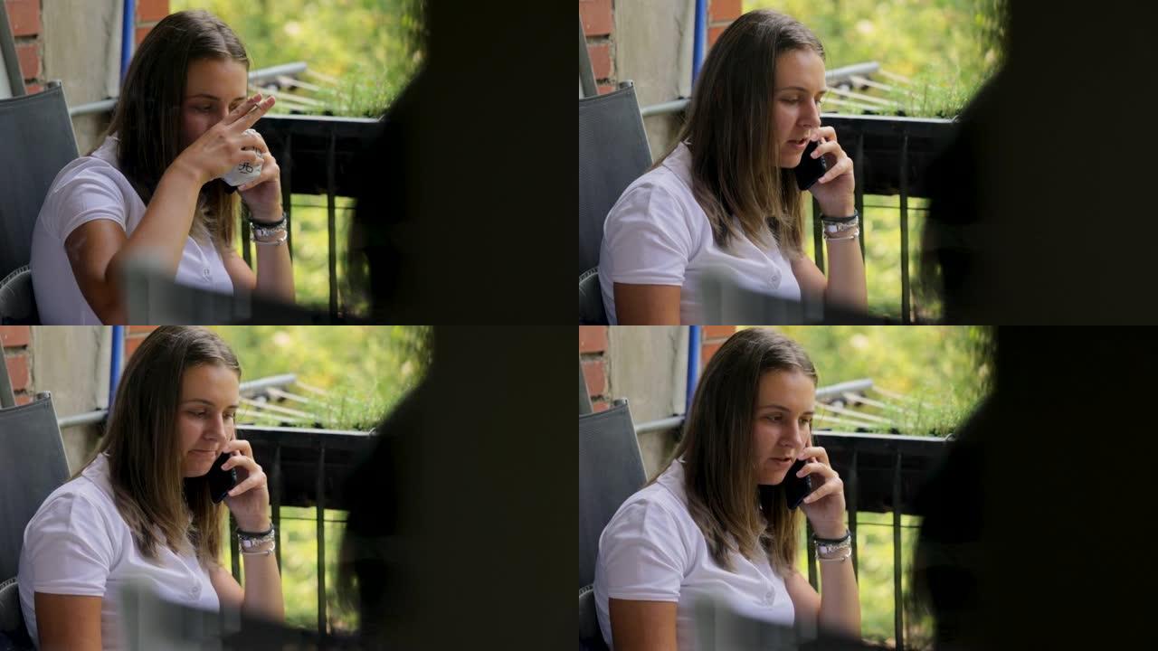 年轻女子在阳台上用手机聊天，同时吸烟和喝咖啡