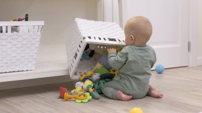 婴儿学会在地板上爬行推翻了一篮子玩具，孩子探索他周围的世界，可爱的7个月大的男婴在家里玩耍。