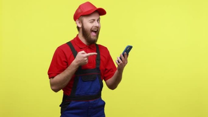 快乐积极的工人男子指着智能手机屏幕，开心地微笑，推荐服务应用程序。