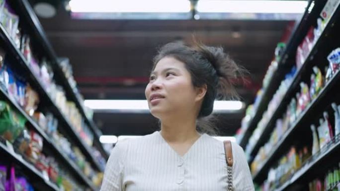 锁定结束，亚洲成年女性享受购物手拉购物车在百货商店的货架上检查消费品