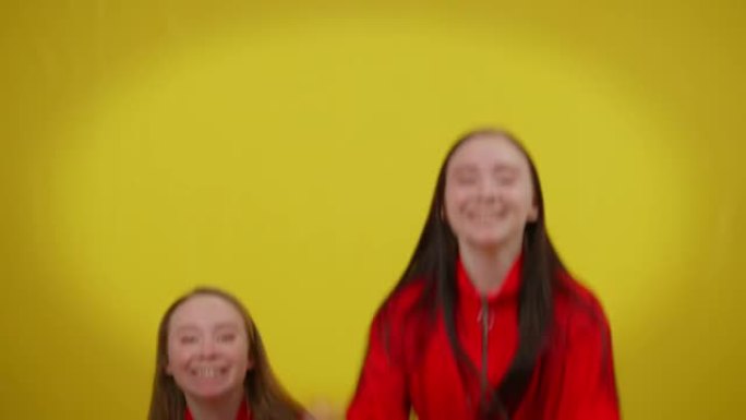 两个快乐兴奋的双胞胎姐妹在黄色背景下跳起来大笑。惊讶的美丽白人苗条女性的前视图看着相机开心