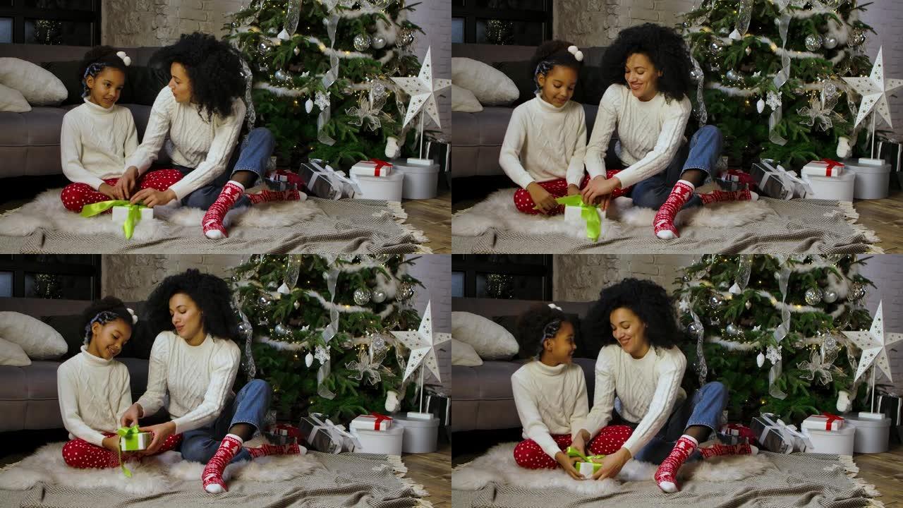 非裔美国妈妈和她的小女儿在礼品盒上系蝴蝶结的肖像。女人和女孩坐在沙发和装饰圣诞树附近。慢动作