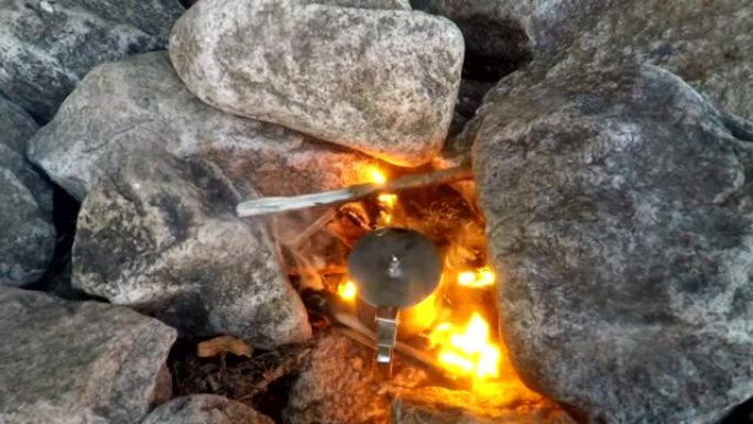 一名男子在石头上的火上加热茶水