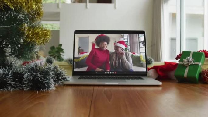 微笑的非洲裔美国母亲和女儿戴着圣诞老人帽子在笔记本电脑上的圣诞节视频通话