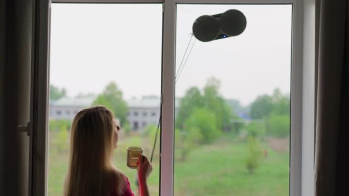 家庭主妇喝茶，看着机器人窗户清洁剂