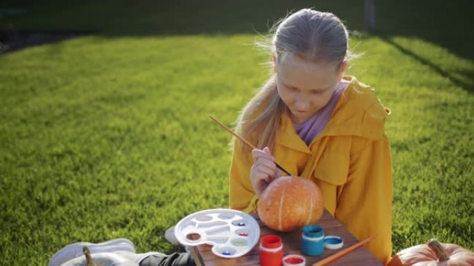 一个孩子画南瓜，为万圣节准备装饰品。坐在房子后院的草坪上