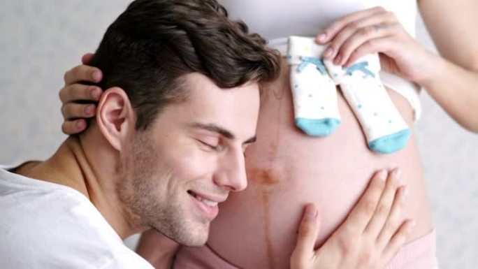 令人惊讶的男人在家里的室内拥抱他可爱的怀孕妻子的腹部