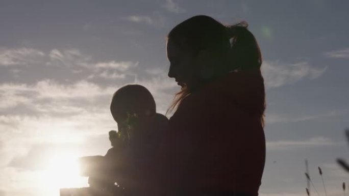 快乐母亲的剪影与他的儿子在夕阳下玩耍，妈妈与婴儿在背光中闪闪发光。