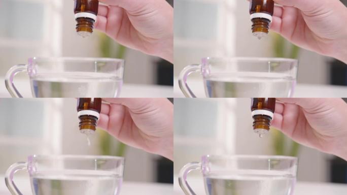 在女性的手特写镜头中，从玻璃瓶中滴入水的药液滴入透明杯中。有人在服用混合物。