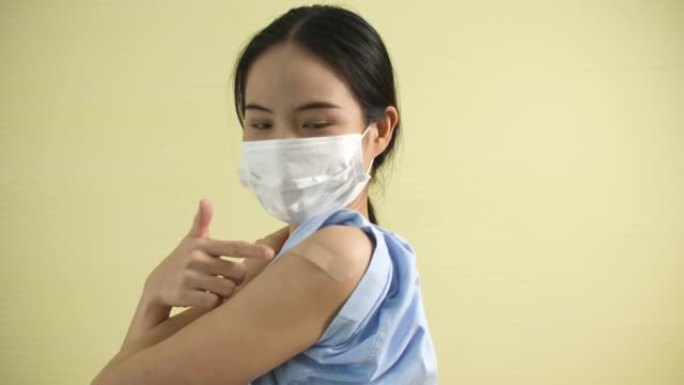 亚洲妇女在接受疫苗后显示并指向手臂上的绷带