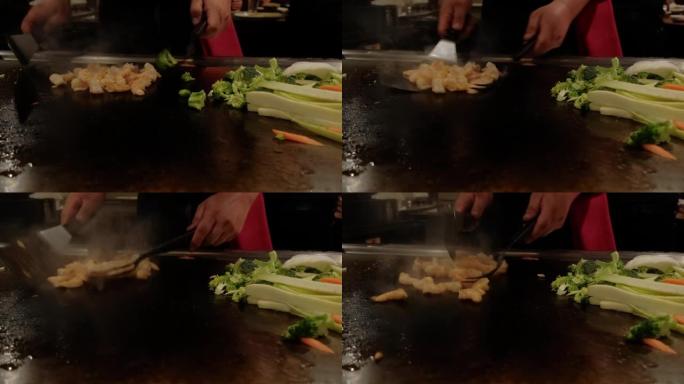特写镜头。日本厨师在hibachi上烹饪铁板烧，海鲜虾和扇贝在热盘上油炸。慢动作