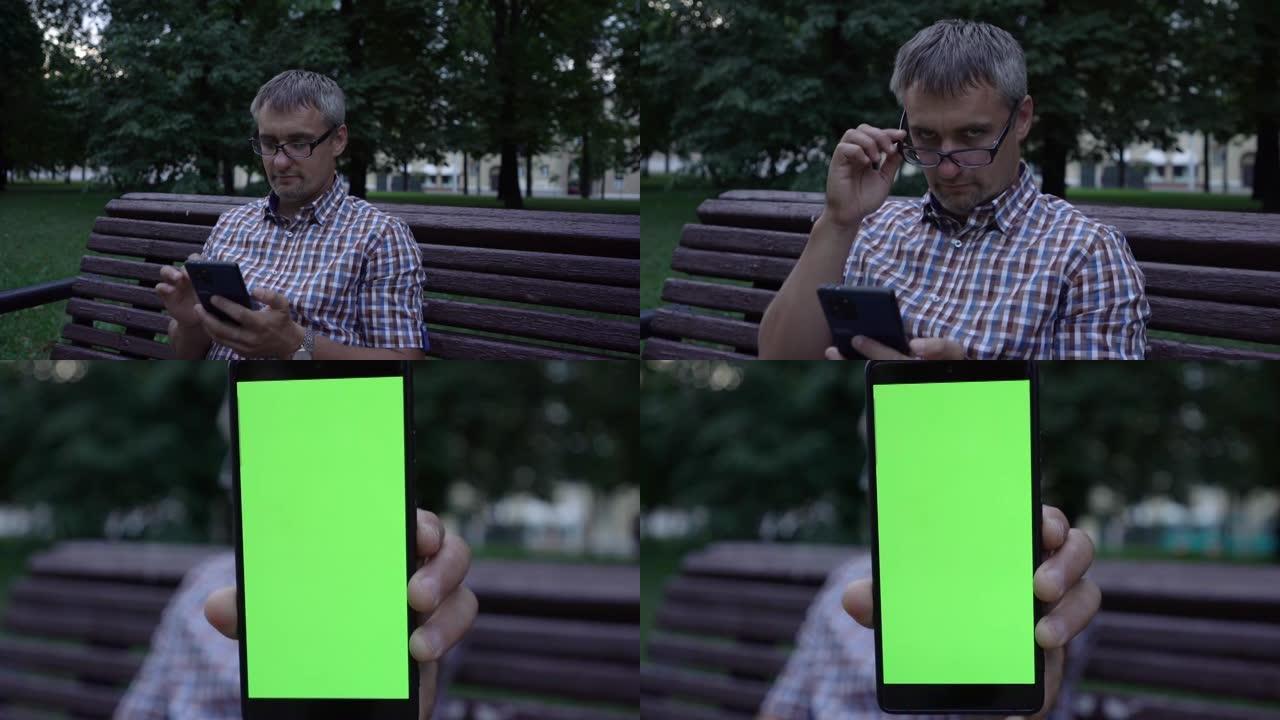 男子展示了带有绿屏的照相手机，并放下了眼镜。