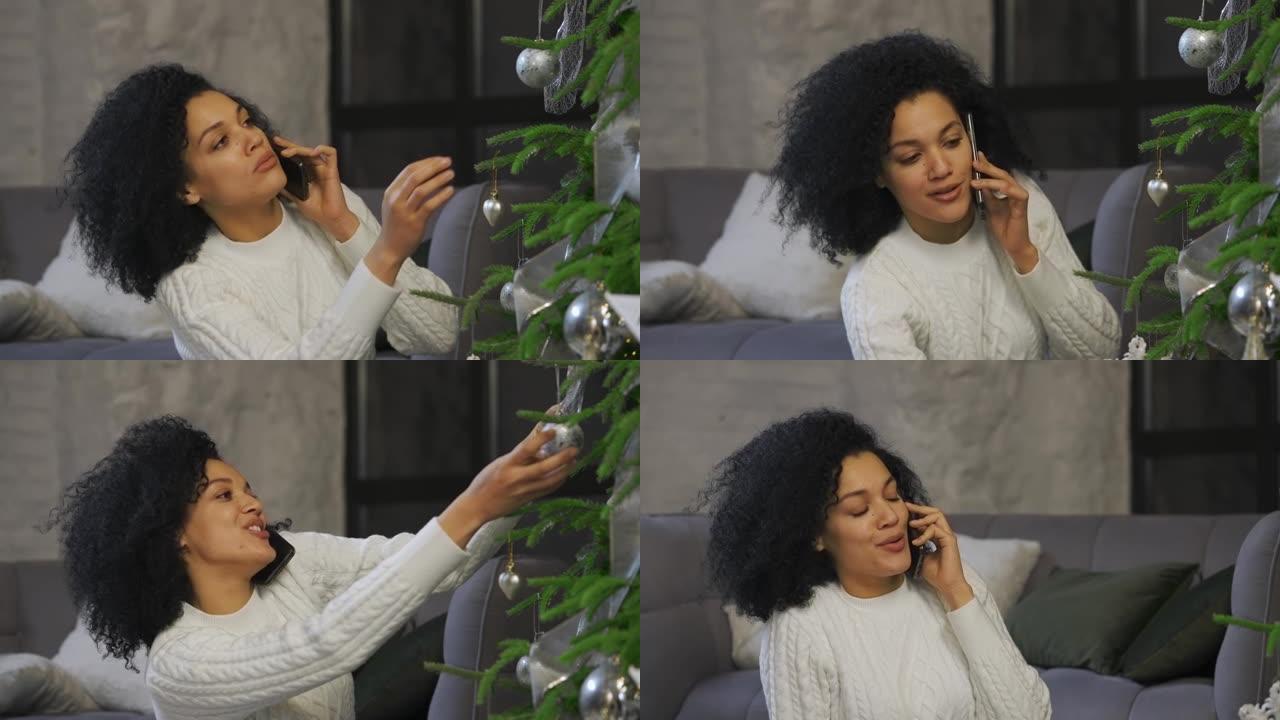 一个快乐的非洲裔美国妇女在智能手机上聊天的肖像。年轻女子坐在明亮的阁楼风格房间里的节日圣诞树旁。节日