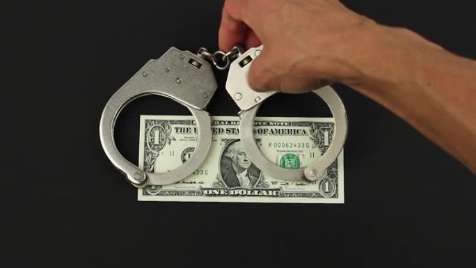汉德把手铐戴在一美元钞票上的黑色背景，金融犯罪或腐败的概念