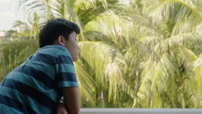 亚洲男孩从酒店的房间阳台上看风景，当到达酒店时，生活方式的概念。