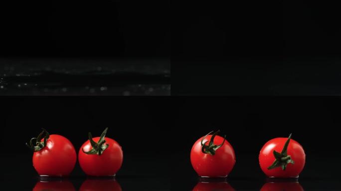 一组视频镜头，两个红色成熟的西红柿，绿色的尾巴落在潮湿的反光桌面上。成熟的樱桃在黑色背景上溅水在桌子