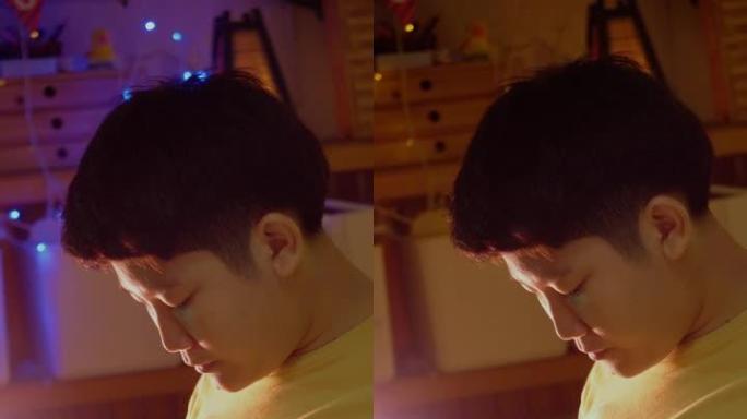 亚洲男孩在晚上在家玩手机游戏，带圣诞灯背景。