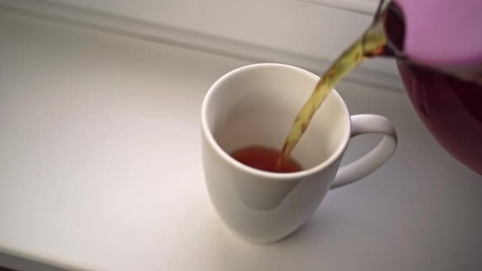 人类将玻璃茶壶中的香茶倒入白色陶瓷杯中。