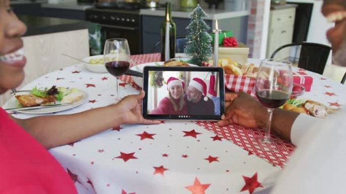 微笑的非洲裔美国夫妇使用平板电脑进行圣诞节视频通话，屏幕上有夫妇