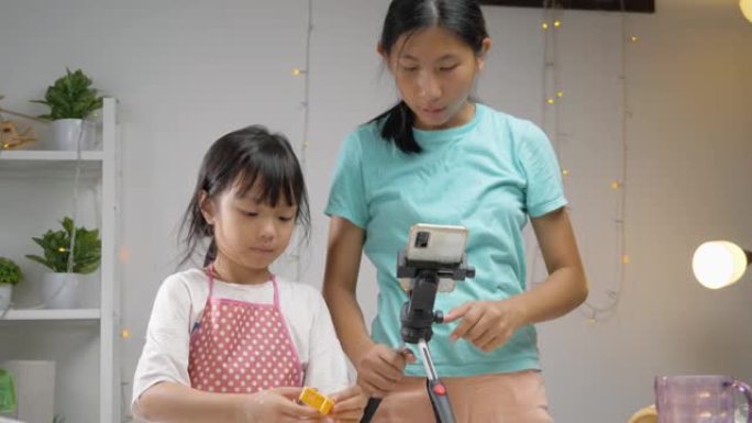 亚洲女孩拍摄视频她的妹妹在家制作自制饼干，用于病毒视频或在家TikTok，新一代概念的时尚生活方式。
