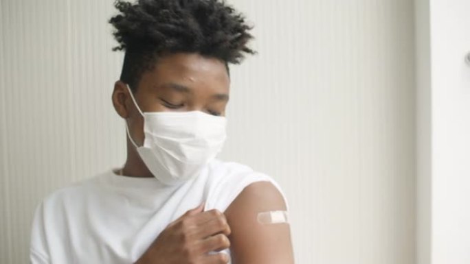 一名非洲裔美国青少年在接种疫苗并在手臂上露出绷带后竖起大拇指的肖像