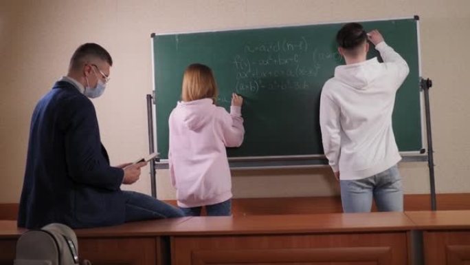 两个学生正站在黑板旁写一个数学方程式。