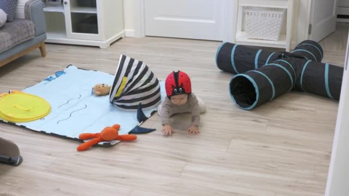 可爱的男婴戴着软安全帽，在家中发现新事物，7个月大的婴儿在地板上玩耍，学习走路，蹲坐和站立。