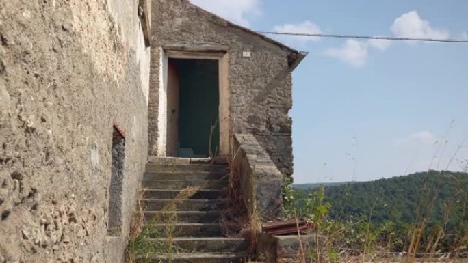 意大利省山区的废弃乡村住宅，破旧的房屋，楼梯上长满了绿色植物，门窗破损，外墙灰泥被毁。战后时期的空h