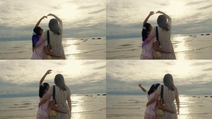 快乐的亚洲母亲和女儿在早晨的阳光下一起在海滩上举起心形的手，生活方式的概念。