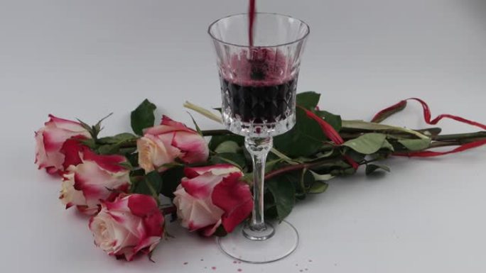 玫瑰花在水晶玻璃杯附近，白色背景上有红酒