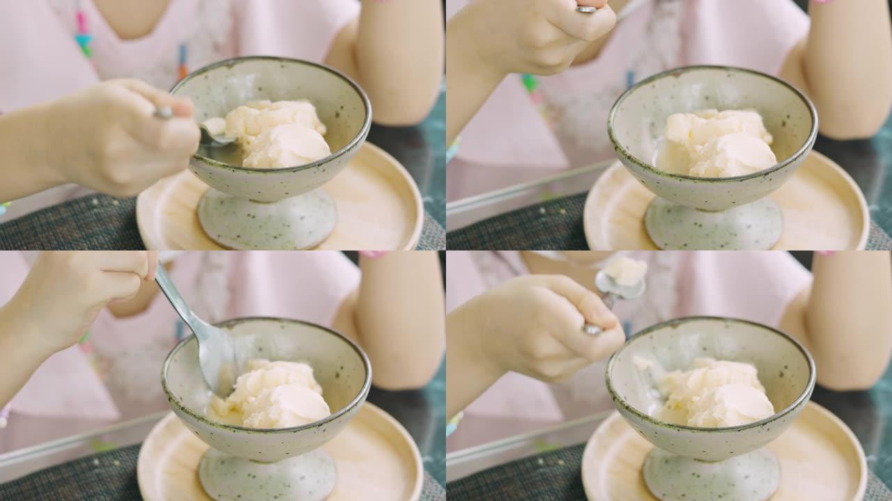 特写4k的无法识别的女孩孩子正在碗里吃香草冰淇淋，它在餐桌上融化，快乐和享受显示了儿童用餐的甜点时间