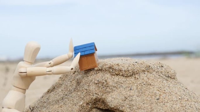 一段延时视频，一个绘画娃娃用手在摇摇欲坠的沙山上抱着倾斜的房子
