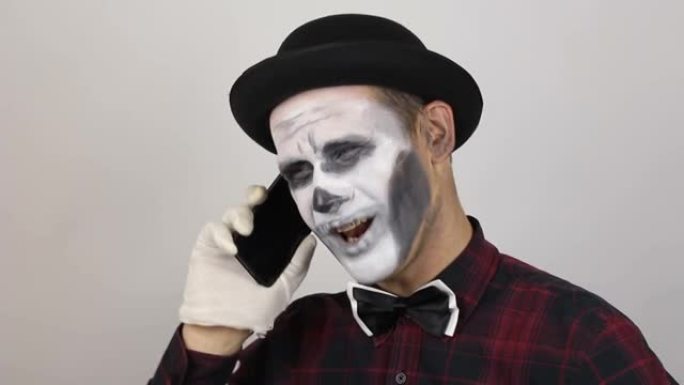 一个穿着小丑妆的可怕男人正在和受害者打手机聊天。一个可怕的小丑正在打电话，笑得很厉害。万圣节服装