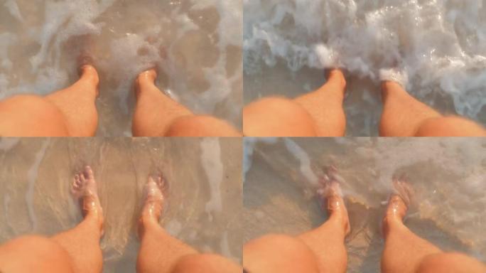 站在飞溅的冲浪中的沙滩上的男性脚的第一人称视角。正上方可见