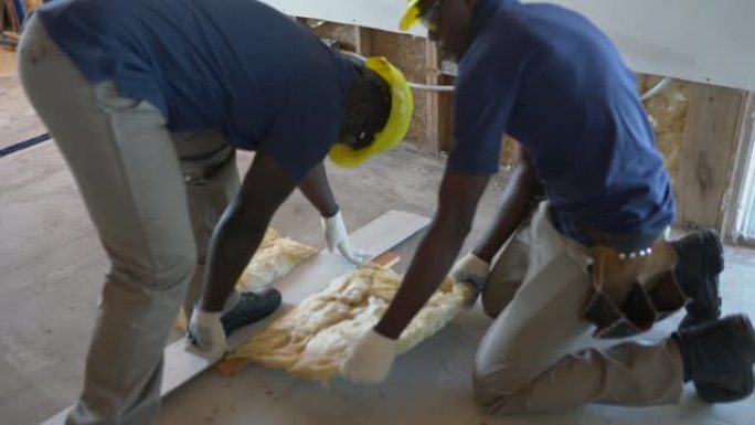 非裔美国建筑工人在木结构房屋建造过程中切割一块玻璃纤维绝缘材料