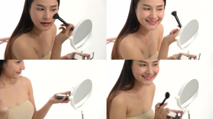 喜欢化妆的亚洲女人。年轻迷人美丽的感觉快乐的样子镜子和脸上的眉毛着色享受白色背景上的美容化妆品