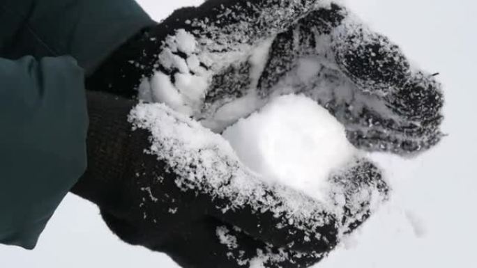戴着黑手套的女性手拿着白雪，冬天在公园里做雪球