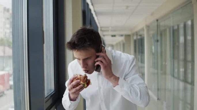 穿白衬衫的年轻人在手机上聊天并在室内吃汉堡