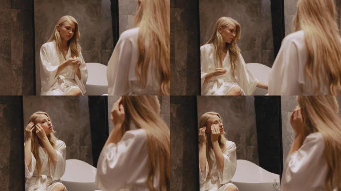 浴室里一个年轻的金发女郎坐在镜子前擦拭她的脸