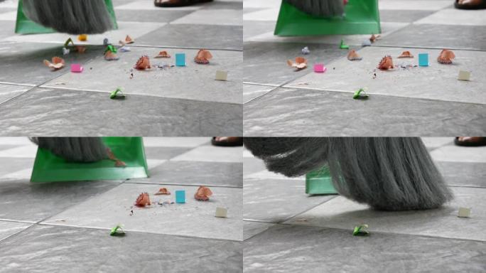 用扫帚和塑料簸箕扫除瓷砖地板上的纸屑和灰尘。