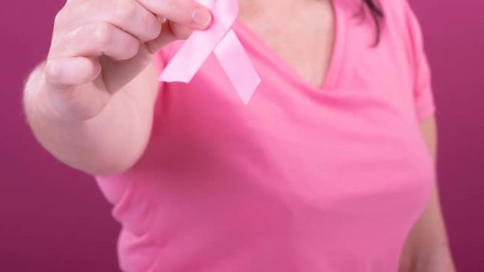 白人妇女手持粉红色癌症意识彩带，背景为粉红色