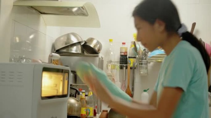 亚洲女孩戴着烤箱手套，将酥皮糕点托盘放入烤箱中，准备在家烘烤。