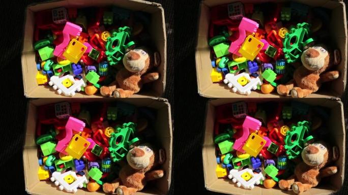 一个装满各种儿童玩具的纸箱。塑料彩色构造器、软熊、娃娃等益智玩具。童年的概念。高清视频镜头。婴儿游戏