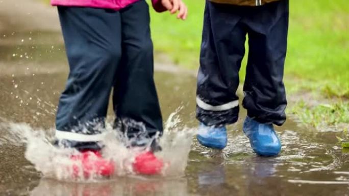 穿着橡胶靴和防水裤的顽皮孩子在雨水坑中跳跃。慢动作