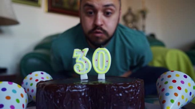 激动的年轻人在家里庆祝自己的30岁生日时，吹着生日蛋糕上的蜡烛