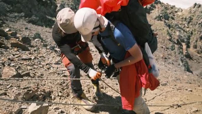 教练将降落器固定在登山者的腰带上，同时在山上艰难的路段上速降。