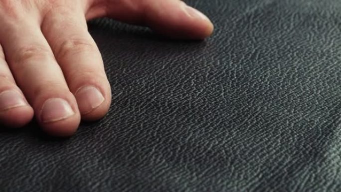 用手特写触摸黑色皮革，生产由真皮或人造革制成的手工配件。工作场所的动物皮肤材料