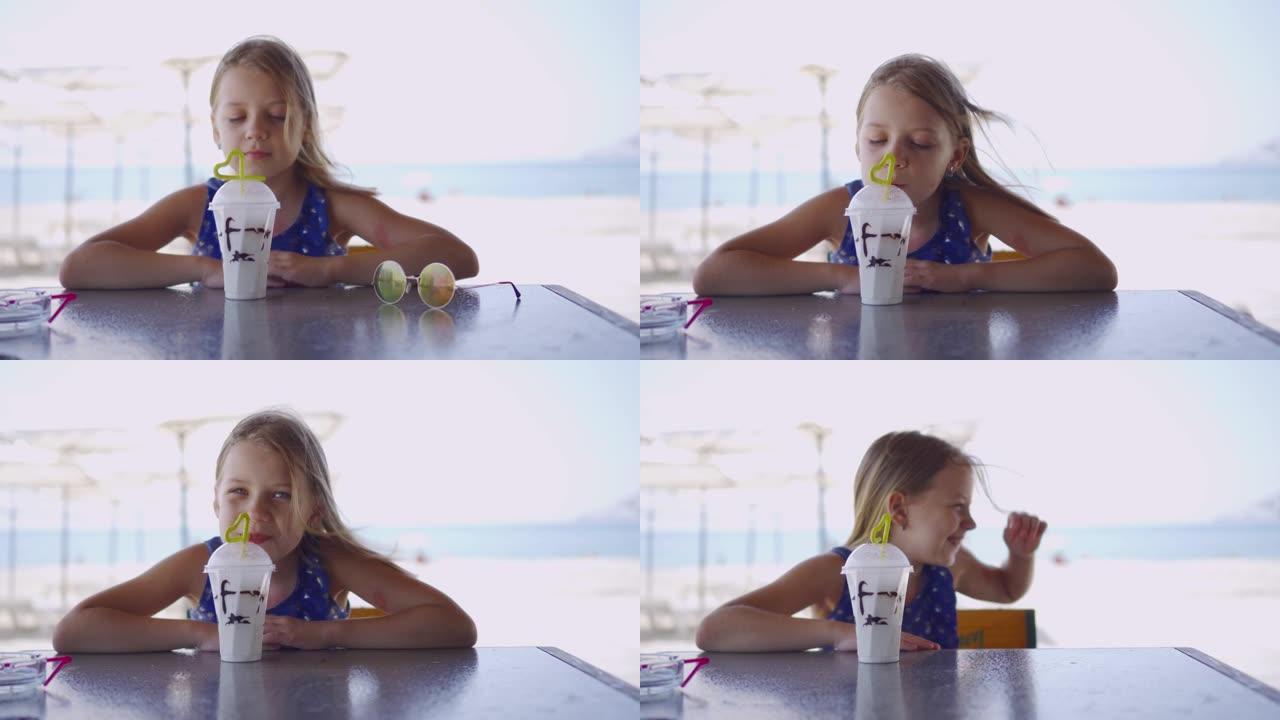 一个开朗，微笑的女孩在暑假期间在海滩上喝清爽的鸡尾酒。眼镜从风中从桌子上掉下来。