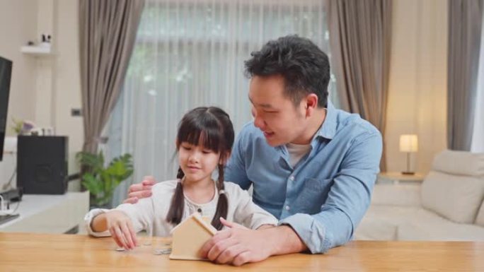快乐的亚洲家庭，慈爱的父亲教导和激励年轻可爱的小女儿为未来省钱。小女孩喜欢和父母一起把硬币放在存钱罐