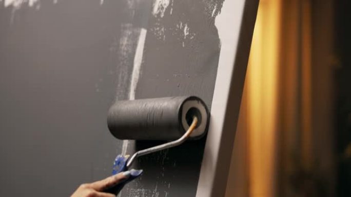 油漆滚筒的特写镜头，手柄上有灰色油漆。一个女人的手握着滚筒，做出精确的动作，一个接一个，上下，用颜色